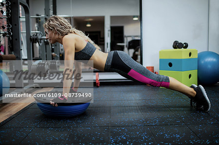 Woman doing push-up on bosu ball in gym