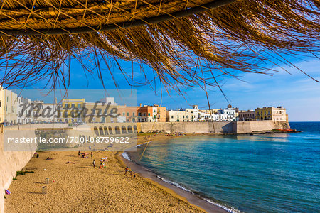 View of the coastal Old Town of Gallipoli from under a straw sun umbrella in Puglia, Italy