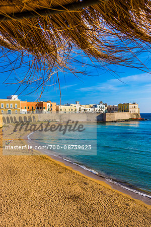 View of the coastal Old Town of Gallipoli from under a straw sun umbrella in Puglia, Italy