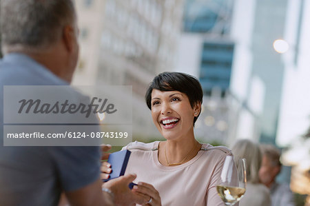 Smiling woman receiving gift from husband at urban sidewalk cafe
