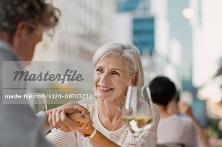 Affectionate senior couple holding hands drinking white wine at urban sidewalk cafe
