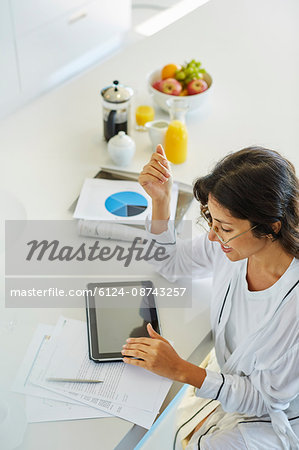 Woman in bathrobe working at digital tablet at kitchen counter