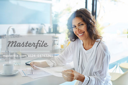 Portrait smiling businesswoman in bathrobe reviewing paperwork in kitchen