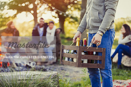 Man carrying crate of wine and beer at campsite with friends