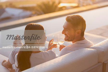 Couple relaxing toasting white wine glasses on chaise lounge on luxury patio