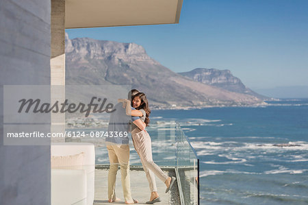 Couple hugging on sunny luxury balcony with ocean and mountain view