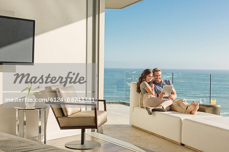 Couple using digital tablet on chaise lounge on sunny luxury balcony with ocean view