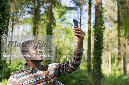 Smiling man taking selfie with camera phone in sunny woods