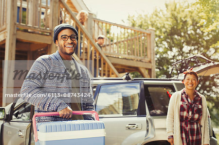 Portrait smiling couple unloading cooler from car outside cabin