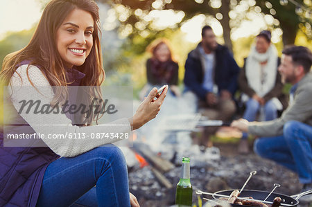 Portrait smiling woman texting and drinking beer at campsite