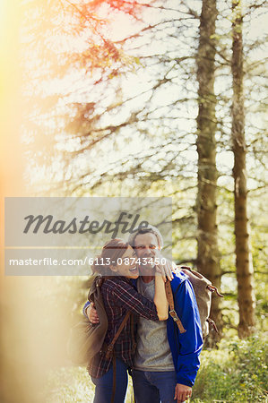 Portrait enthusiastic couple with backpacks hiking in sunny woods