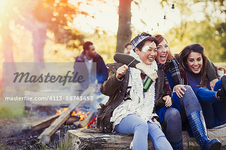 Friends laughing roasting marshmallows at campfire