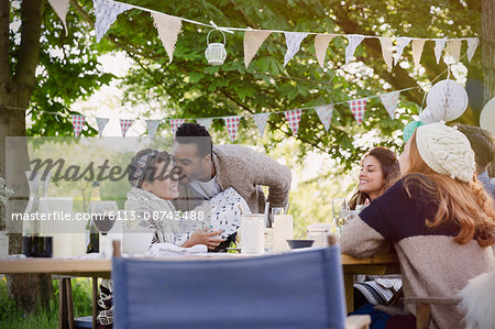 Boyfriend kissing girlfriend with birthday gift at garden party table