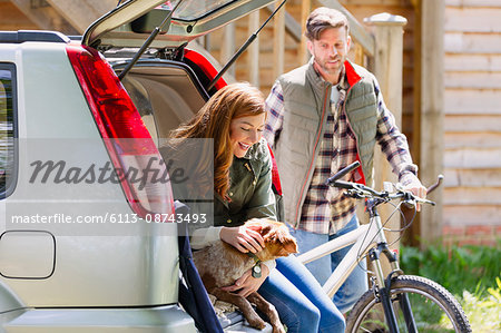 Couple with dog and mountain bike at back of car outside cabin