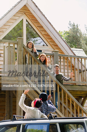 Friends on stairs waving to friends in car outside sunny cabin