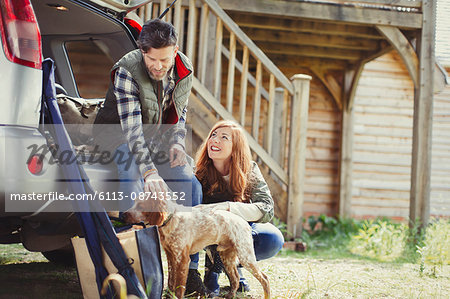 Couple with dog at back of car outside cabin