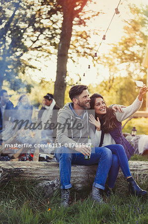 Couple posing for selfie with camera phone near campfire