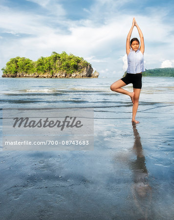 Thai girl doing a yoga position (tree pose) on Nopparat Thara Beach in Krabi Thailand.