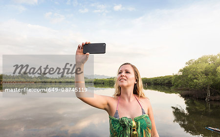 Young woman taking smartphone selfie in front of lake, Gili Meno, Lombok, Indonesia