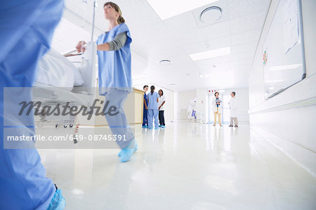 Male and female medics urgently pushing hospital bed along corridor