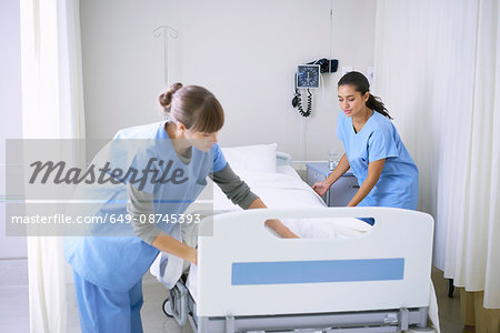 Two female nurses making hospital bed in ward