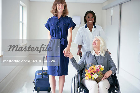 Daughter and hospital orderly pushing senior female patient in wheelchair