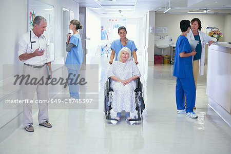 Nurse pushing senior female patient in wheelchair onto hospital ward