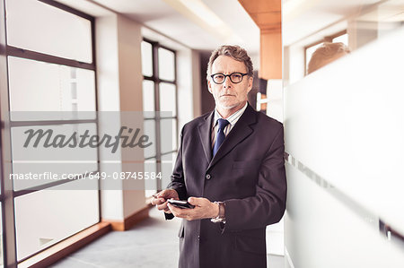 Portrait of senior businessman at office doorway using smartphone