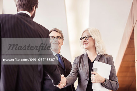 Businessmen and woman shaking hands in office corridor