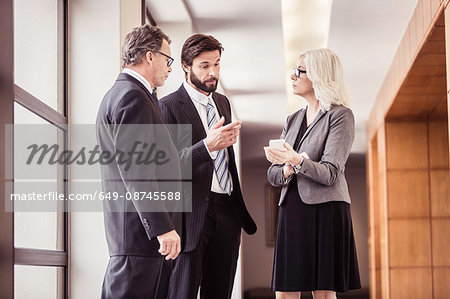 Businessmen and woman having discussions in office corridor