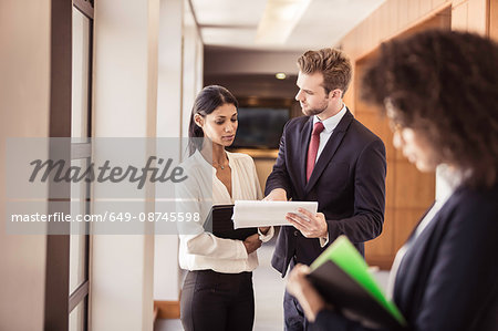 Young businesswoman and businessman reading paperwork in office corridor