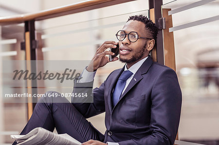 Businessman sitting on floor chatting on smartphone on office balcony