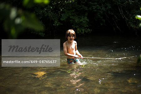 Boy waist deep in water holding stick