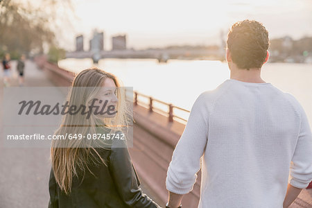 Rear view of couple strolling on waterfront at sunset, Battersea Park, London, UK
