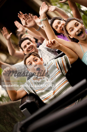 Smiling family riding on a rollercoaster at an amusement park.