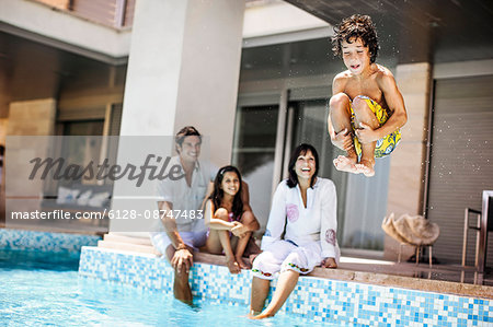Young boy cannonballs into a pool while his smiling family watch.