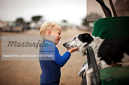 Little boy wearing wetsuit patting dog on the beach