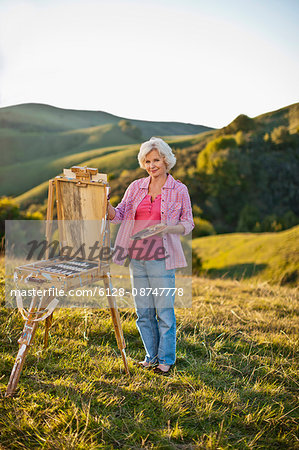 Mature woman painting on a scenic hillside.