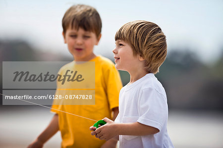 Two young boys flying a kite at the beach.