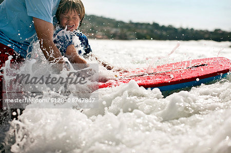 Father teaching young son how to ride a wave on a boogie board.