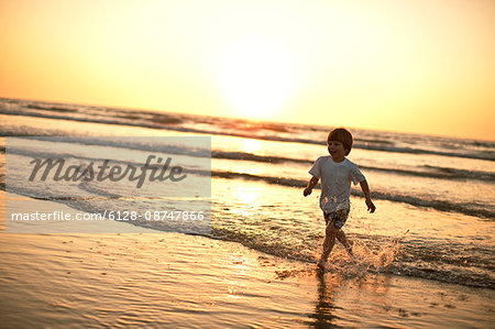 Preschool age boy running along the beach at sunset.
