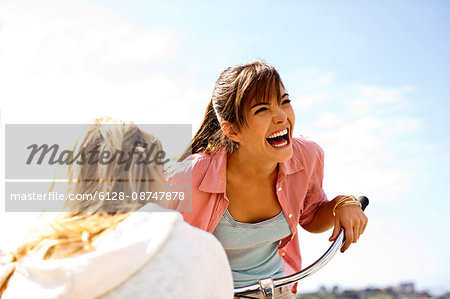 Girl on a bicycle,  laughing with her friend.