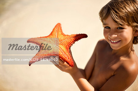 Portrait of a smiling young boy showing off a starfish that he has found.