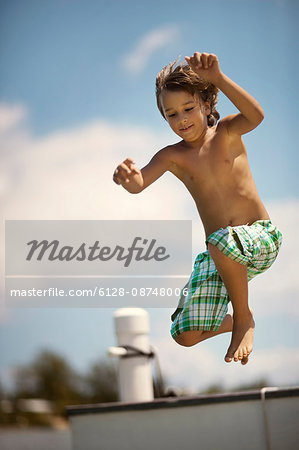 Smiling young boy leaping from a pier into the water.