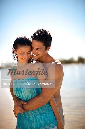 Happy young honeymoon couple share a romantic embrace on a sunny tropical beach.