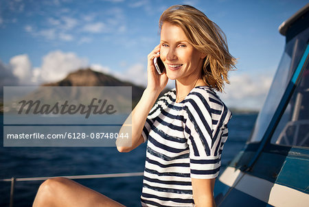 Mid-adult woman with wind-swept hair talking on cell phone on boat.