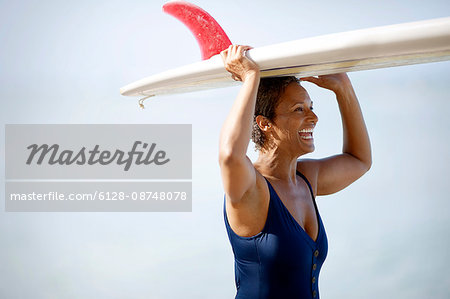 Woman holding surf board above her head.