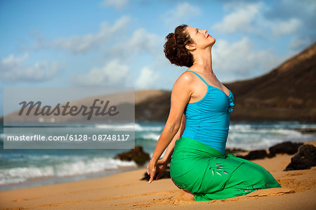 Serene mid-adult woman practicing yoga on a beach.