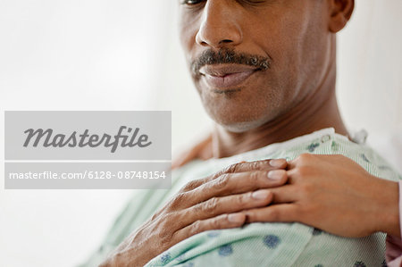 Hospital patient touches the comforting hand laid on his shoulder.