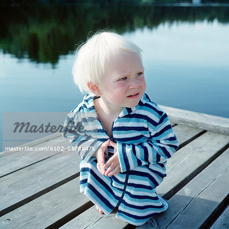 Boy in bathrobe sitting on jetty